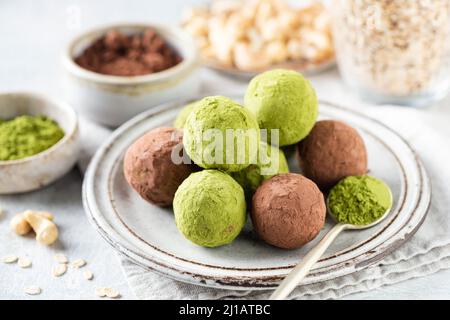 Hausgemachter grüner Matcha und Johannisbrottrüffel auf dem Teller mit Nüssen, Datteln und Haferflocken. Gesunde, zuckerfreie vegane Paleo-Trüffel Stockfoto