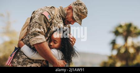 Liebevolles militärisches Wiedersehen zwischen Vater und Tochter. Emotionaler Militärvater umarmt seine Tochter auf seiner Heimkehr. Armeesoldat erhält ein w Stockfoto