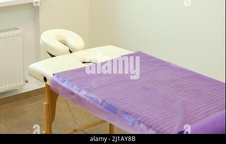 Beigefarbener Massageliegen mit einem Einwegtuch bedeckt. Massageliege mit Kopfstütze in einem Massageraum Stockfoto