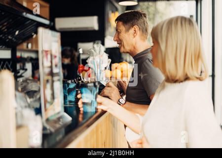 Ein erwachsenes, reifes, glückliches Paar, verliebt in einem Straßencafe, bestellt Kaffee. Ein blonder Kaukasusmann und eine blonde Frau verbringen Zeit miteinander. Ältere Frau und Ehemann Stockfoto