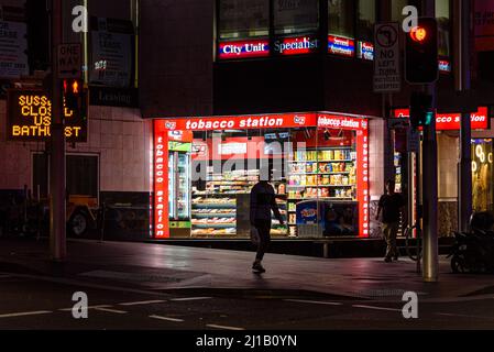 Ein Mann, der nachts vor einem Tabakladen im CBD von Sydney läuft Stockfoto