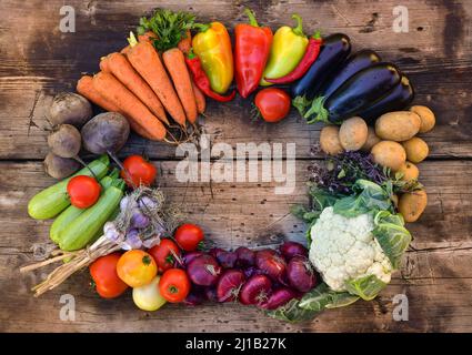 Eine Ernte von Gemüse, die in Form eines ovalen Rahmens auf einem hölzernen Hintergrund ausgelegt ist. Stockfoto