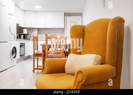 Ein Ockergelber Ohrensessel im Wohnzimmer neben einer offenen Küche Stockfoto