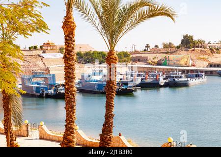 Blick auf das Dorf Abu Simbel an sonnigen Tagen in Assuan, Oberägypten, mit den Schiffen im Nasser-See und den massiven Felsentempeln im Backgr Stockfoto