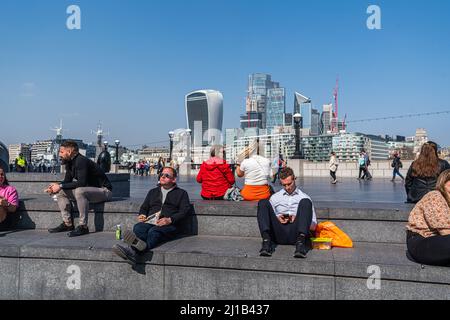 LONDON, GROSSBRITANNIEN. 24 März, 2022 . Büroangestellte sitzen in der Frühlingssonne an der Schaufel am Londoner Flussufer zur Mittagszeit, da das warme Wetter anhält und mit hohen Temperaturen von 20 grad celsius bis zum Wochenende andauern wird. Zum ersten Mal seit August 2020 wird in London eine Warnung vor hoher Luftverschmutzung ausgegeben. Kredit: amer ghazzal/Alamy Live Nachrichten Stockfoto