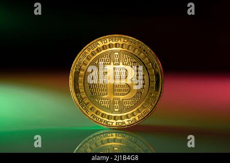 Bitcoin BTC Kryptowährung physische Münze auf der reflektierenden Oberfläche platziert und mit grünen und rosa Lichtern beleuchtet. Stockfoto