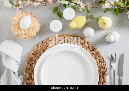 Ostertisch mit gelbem Küken, Bio-Eiern, frischen Blumen auf Leinentischdecke. Blick von oben. Christliche Tradition. Stockfoto