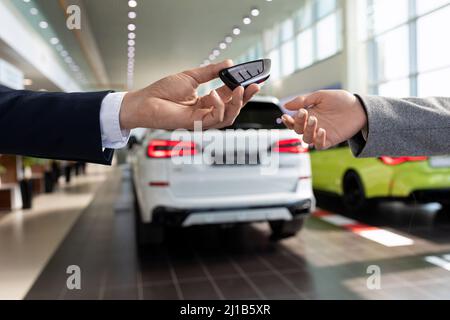 Ein Mitarbeiter eines Autohauses übergibt vor dem Hintergrund des Ausstellungsraums die Schlüssel für ein neues Auto aus nächster Nähe an einen Käufer Stockfoto