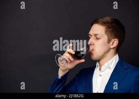 Männlicher Sommelier, der Rotwein im Anzug auf schwarzem Hintergrund verkostet. Weinherstellung. Berufe Stockfoto