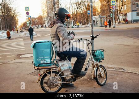 Moskau, Russland - 25. Februar 2022: Yandex lavka Kurier auf behelfsmäßigen Moped hielt an der Ampel, um die korrekte Lieferadresse zu überprüfen. Stockfoto