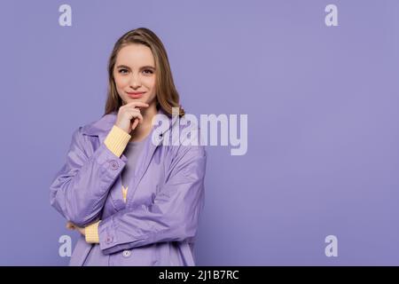 Zufrieden junge Frau in Trenchcoat isoliert auf lila Stockfoto