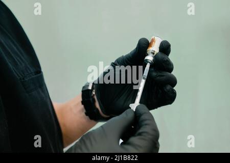 Nahaufnahme eines Arztes mit schwarzen Peelings und Handschuhen, die vor hellgrünem Hintergrund eine medizinische Spritze füllen Stockfoto