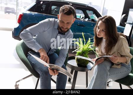 Ein verheiratetes Paar, das in einem Autohaus sitzt, wählt ein neues Auto aus dem Katalog Stockfoto