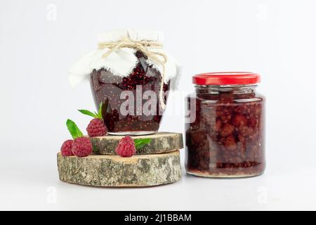 Himbeermarmelade in Gläsern und frische Himbeeren mit Minzblättern auf weißem Hintergrund Stockfoto