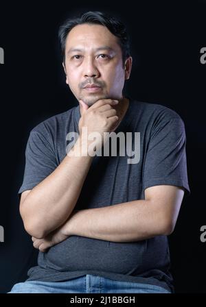 Intelligenter Mann mittleren Alters mit Bärtigen, der ein graues T-Shirt auf schwarzem Hintergrund trägt. Denkkonzept Stockfoto