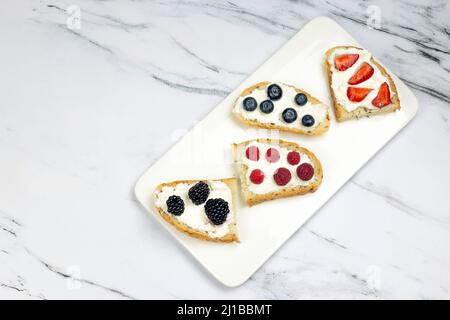 Leckeres Toastbrot mit Frischkäse, Erdbeere, Himbeere, Brombeere und Heidelbeere auf weißem Marmorboden. Morgen, Frühstückskonzept, Draufsicht, Stockfoto
