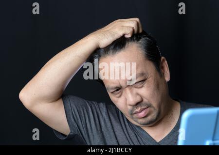 Ein Mann mittleren Alters scheint im Spiegel und sorgt sich um Haarausfall oder Haargrau Stockfoto