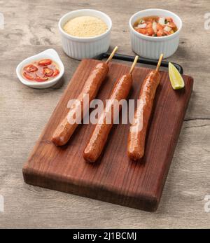 Schweinewurstspieße auf Holzbrett mit Farofa, Zitrone und Vinaigrette. Stockfoto