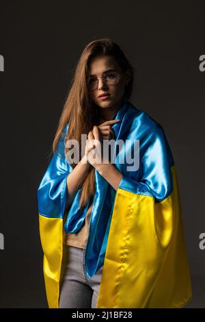 Traurige Frau mit Ukraine-Flagge bedeckt. Konzept des Stehens mit der ukrainischen Nation im Krieg mit Russland. Stockfoto