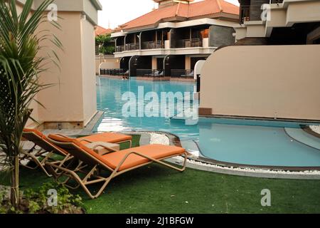 Am Abend nach Sonnenuntergang stehen zwei orangefarbene Sonnenliegen am leeren Pool Stockfoto