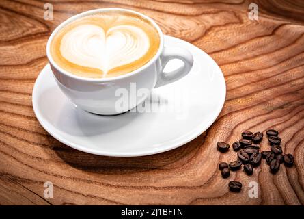 Tasse Kaffee Latte mit herzförmiger Milch, Kaffeebohnen auf dem Tisch Stockfoto