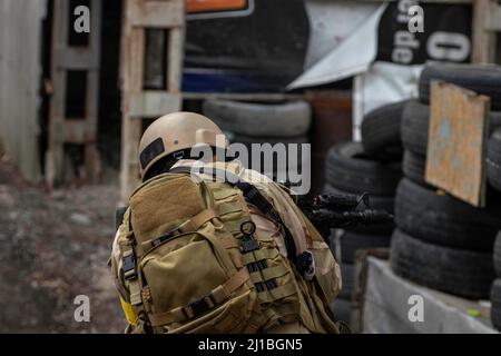 airsoft Spiel, ein Spieler in einer Uniform und in einem Helm mit einer Airsoft-Waffe, auf einem speziellen Spielplatz, mit Unterständen von alten Rädern Stockfoto