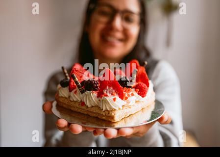 Junge lächelnde Frau mit herzförmigem Kuchen mit roten reifen Erdbeeren und frischen Himbeeren und Heidelbeeren. Valentinstag, Muttertag, OP Stockfoto