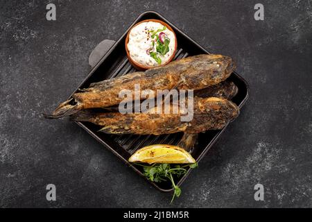 Gebratener Fisch Schwarzmeerwürfel, mit Zitrone und Kräutern, auf dunklem Grund Stockfoto