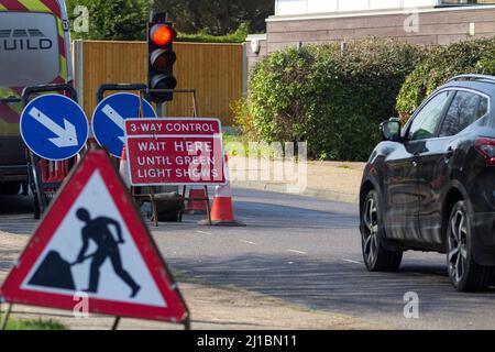 Ampelkontrolle bei Straßenarbeiten 3-Wege-System, Männer bei der Arbeit Zeichen, weiße Pfeile auf blauen Hintergründen, rote warten hier Zeichen Verkehr Kegel warten Fahrzeug Stockfoto