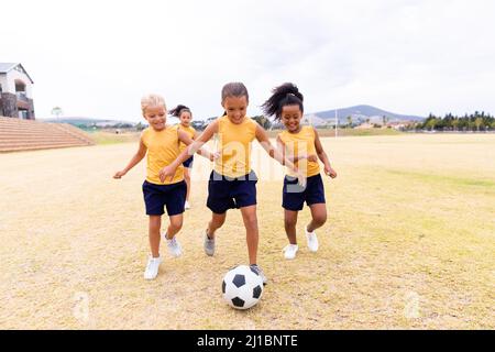 Die ganze Länge der multirassischen Grundschüler, die auf dem Schulgelände Fußball spielen Stockfoto