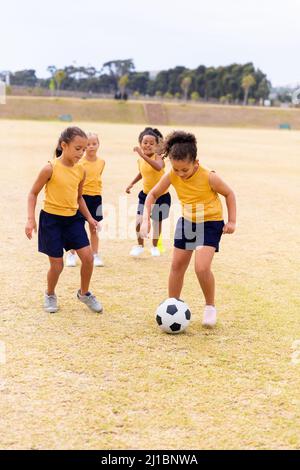 Die gesamte Länge der multirassischen Grundschüler läuft beim Fußballspielen auf dem Schulgelände Stockfoto