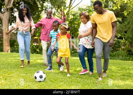 Glückliche afroamerikanische Familie mit mehreren Generationen, die am Wochenende im Hinterhof Fußball spielt Stockfoto