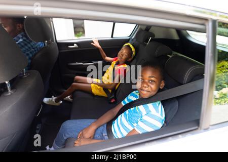 Porträt eines lächelnden afroamerikanischen Bruders und einer Schwester mit Sicherheitsgurten, die im Auto unterwegs sind Stockfoto