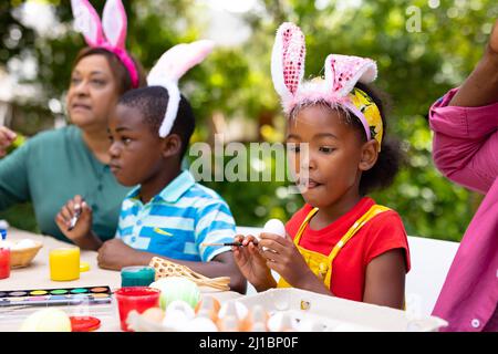 afroamerikanisches Mädchen trägt Hasen Ohren Malerei Eier mit Familie im Hinterhof am ostertag Stockfoto