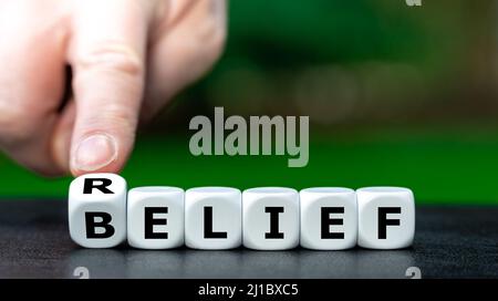 Symbol für die Erleichterung durch Religion. Die Hand dreht Würfel und ändert das Wort Glaube in Erleichterung. Stockfoto