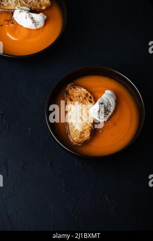 Butternut-Kürbissuppe mit Rahm- und Parmesan-Toasts in Keramikschale auf dunklem Hintergrund, herbstlich gemütliches vegetarisches Gericht, Draufsicht Stockfoto