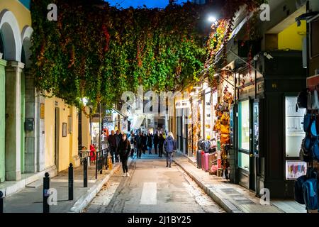 Eine malerische Straße im Plaka-Viertel von Athen, Griechenland, die am Abend mit Pflanzen und blühenden Bäumen beleuchtet wurde. Stockfoto