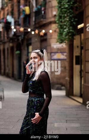 Alternative Frau lächelt, während sie draußen auf der Straße telefoniert. Stockfoto