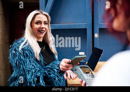 Frau, die in einem Café kontaktlos mit einem Mobiltelefon bezahlt. Stockfoto