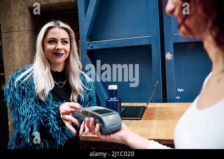 Frau, die mit einer Kreditkarte am kabellosen POS-Terminal in einem Café bezahlt. Stockfoto