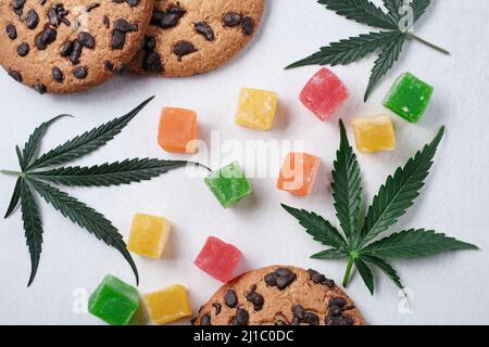 Marmelade und amerikanische Kekse mit Cannabisextrakt. Süßigkeiten mit CBD-Öl. Marihuana Blätter auf weißem Hintergrund. Draufsicht, flach liegend. Stockfoto