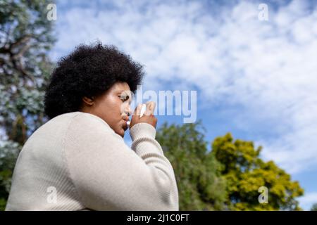 Aus der Perspektive einer afroamerikanischen Frau mit mittlerem Erwachsenen, die Asthma-Inhalator verwendet, während sie gegen den Himmel steht Stockfoto