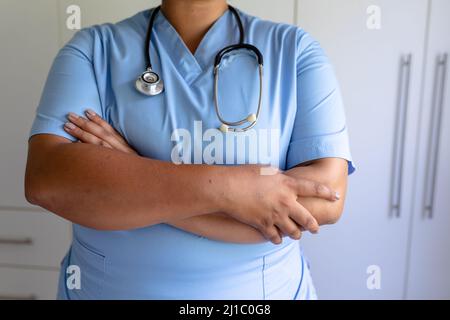 Mittelteil einer afroamerikanischen Krankenschwester mit mittlerem Erwachsenen, die mit gekreuzten Armen und Stethoskop steht Stockfoto