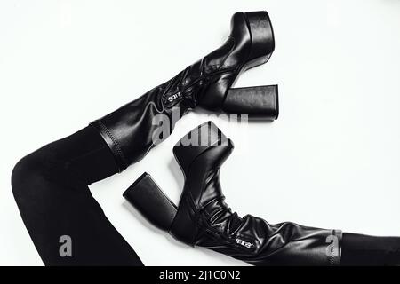 Schlanke Damenbeine in schwarzen Lederstiefeln auf weißem Hintergrund. Modische Schuhe auf hoher Plattform. Trendige Bots-Kollektion für die starken Frauen von heute. Hintergrund. Stockfoto