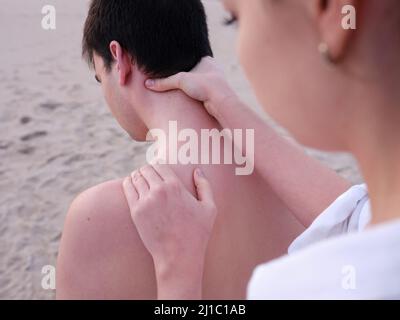Eine junge Chiromassage-Therapeutin, die einem jungen Mann an einem Strand in Valencia Schulter- und Nackenmassagen gibt. Stockfoto