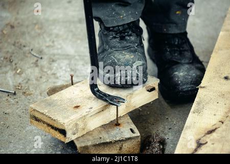 Arbeiter in rauen Stiefeln zieht Nägel aus Holzbohlen. Bau und Reparatur. Hintergrund. Stockfoto