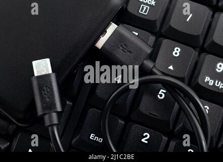 Powerbank zum Laden eines schwarzen Smartphones liegt auf einer kabellosen Tastatur. Powerbank aus nächster Nähe Stockfoto