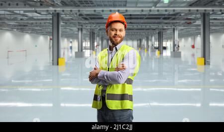 Ingenieur mit reflektierender Weste und Helm, der in einer Halle posiert Stockfoto