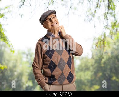 Älterer Mann, der in einem Park mit Bäumen an seinem Hals juckt Stockfoto