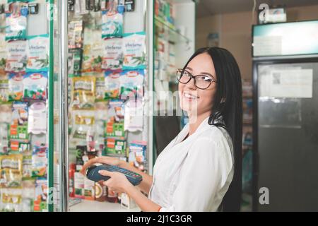 Apotheke und der Verkäufer. Eine Frau in einer Brille mit einem Lächeln kauft über ein mobiles Endgerät mit einer Bankkarte. Speicherplatz kopieren. Stockfoto